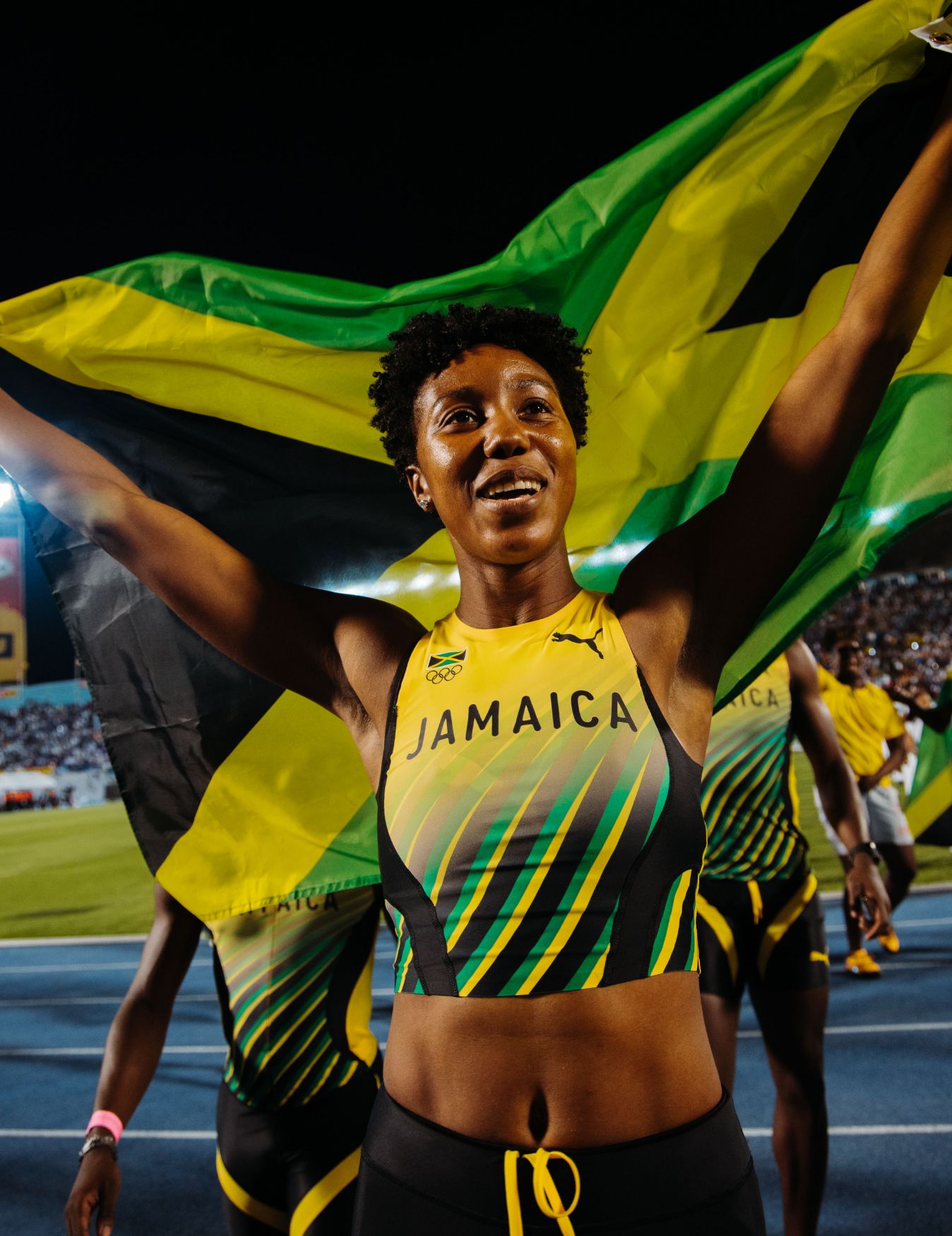 Shanieka Ricketts at the Olympic Games, raising the Jamaican flag for her team behind her.