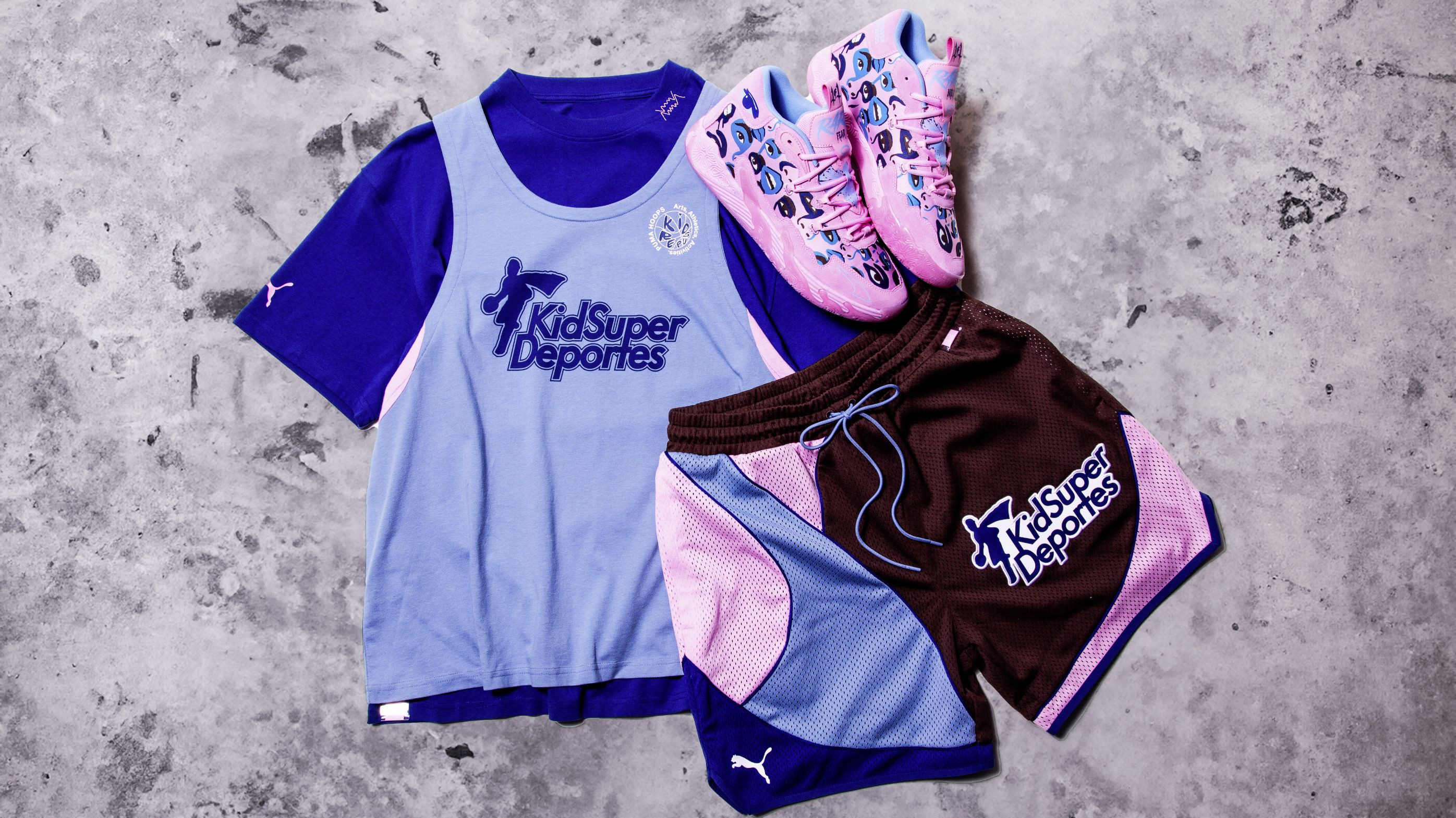 PUMA x KIDSUPER Sportswear set, in shades of blue, rose and brown, of a T-shirt layered with a tanktop, combined with shorts and trainers with comicstyle prints.